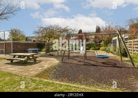 Empty playground with wooden picnic table and various play equipment surrounded with trees against cloudy sky during sunny day Stock Photo