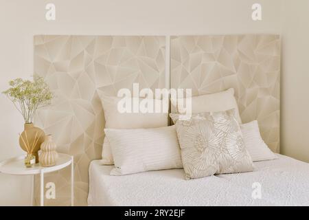 Interior of stylish bedroom with cozy bed and pillows with decorated wallpaper at home with decors on table Stock Photo