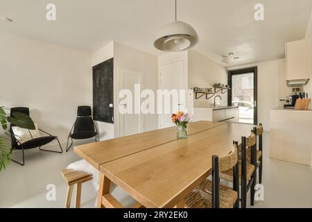Wooden dining table and chairs arranged in front of open plan kitchen with blackboard on wall in corner at modern spacious apartment Stock Photo