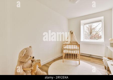 Interior of spacious nursery with wooden crib and soft teddy bear next to radiator and bright window in modern apartment Stock Photo