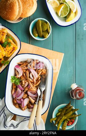 Pulled bbq chicken with baked onions on serving platter, bbq corn, pickles, chili peppers and buns for hot dogs and burgers, tomato sauce. Traditional Stock Photo