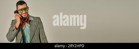 joyful man in plaid jacket and sunglasses talking on retro phone on grey, vintage fashion, banner Stock Photo