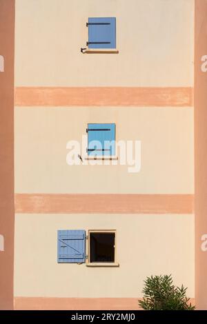 Two closed and one open blue shuttered windows on a wall in Le Barcares, France Stock Photo
