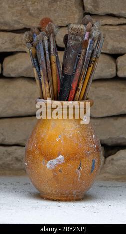 A bowl full of old and worn paint brushes with paint stains on them. Stock Photo