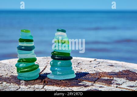 Wet colored glass sea stones arranged in balanced pyramids on a wooden surface against a blue sea background Stock Photo