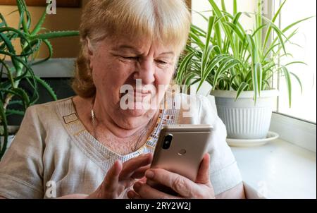 Senior woman using smartphone and smiling while sitting at home Stock Photo
