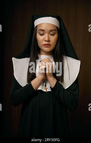 Portrait of religious nun praying with eyes closed holding crucifix rosary Stock Photo