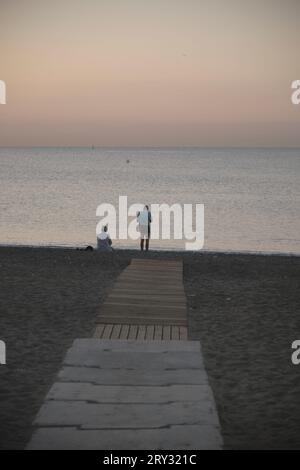 Couple at the end of the walkway on the sand by the sea sunrise Stock Photo