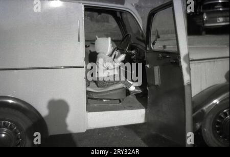1960s, historical, a young child sitting in the driver's seat of a small delivery van holding the large metal steering wheel, pretending to drive, England, UK. Stock Photo