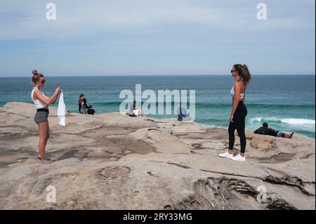 27.09.2019, Sydney, New South Wales, Australia - Young woman photographs her friend on the cliffs at Tamarama Point along Bondi to Bronte Coastal Walk. Stock Photo