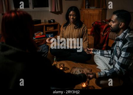 Multiracial friends holding hands sitting with ouija board in log cabin Stock Photo