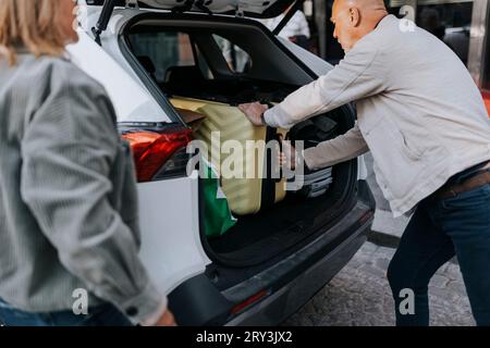 Side view of elderly man loading suitcase in car trunk Stock Photo