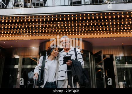 Smiling senior man sharing smart phone with female elderly friend outside movie theater Stock Photo
