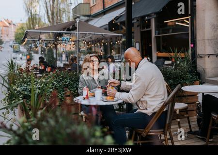 Happy male and female senior friends talking to each other while having food at sidewalk cafe Stock Photo