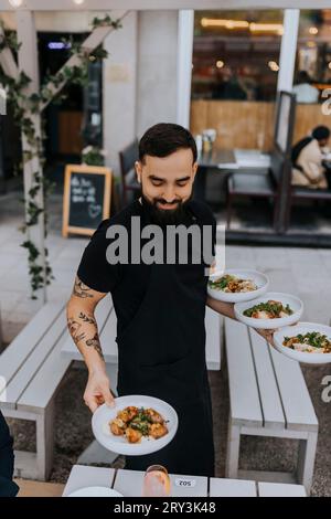 Smiling young male waiter serving food at restaurant Stock Photo