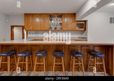 Bar Style Kitchenette with Six Bar Stolls and Long Island Counter. Wood Cabinets and Minimal Styling Stock Photo