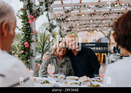 Portrait of smiling senior man with arm around elderly female friend sitting at restaurant Stock Photo