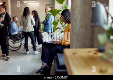 Businesswoman using laptop while sitting near colleagues at office Stock Photo