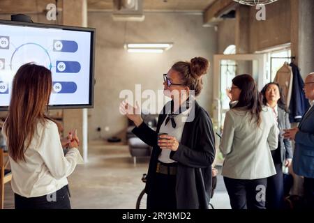 Businesswomen discussing by television near colleagues in office Stock Photo