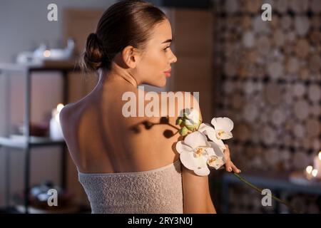 Pretty young woman with orchid flowers in spa salon Stock Photo