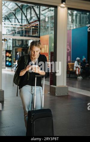 Woman using smart phone while standing with luggage at station Stock Photo