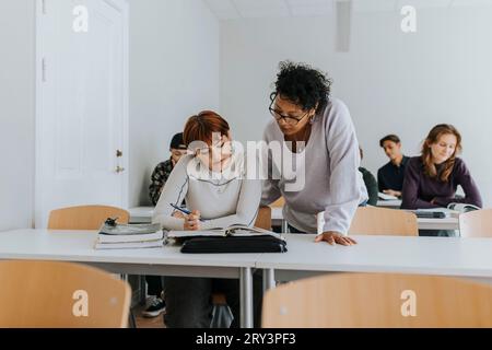 Mature female teacher assisting teenage student at desk in classroom Stock Photo