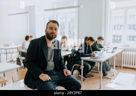 Portrait of bearded male professor sitting on desk in classroom Stock Photo