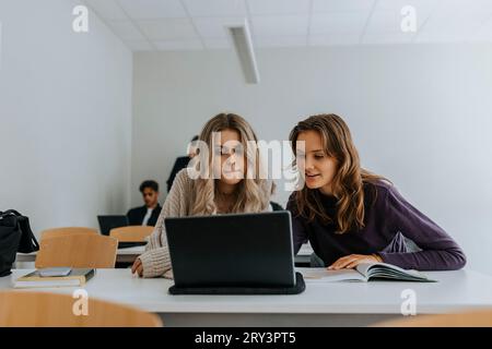 Young female students using laptop together at desk in classroom Stock Photo