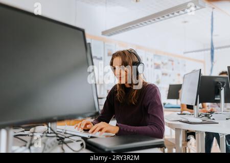 Young woman listening through headphones while using computer in school lab Stock Photo