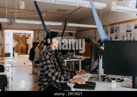 Young man using computer while listening through headphones in lab Stock Photo