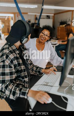 Smiling teacher looking at young male student in computer lab Stock Photo
