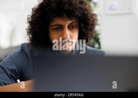 Focused arab entrepreneur working at financial data and analyzing report on laptop. Concentrated start up company man employee planning marketing strategy in business office Stock Photo