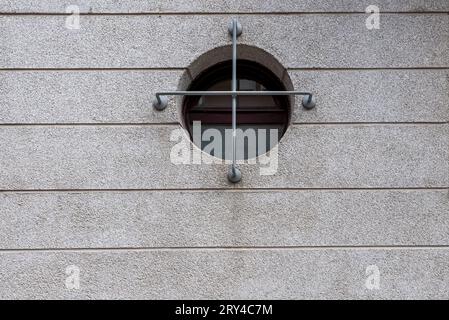 A cement wall with a porthole window with a gray painted cross grille Stock Photo