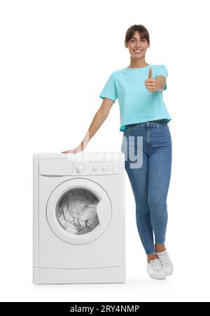 Beautiful woman showing thumbs up near washing machine with laundry on white background Stock Photo