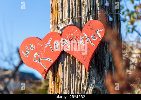 Two painted red hearts with the words 'We R together' displayed on a wooden pole in Vancouver, Canada Stock Photo