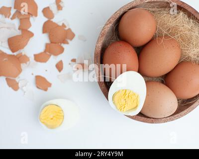 boiled chicken eggs in a wooden bowl isolated on white, one of which is peeled Stock Photo
