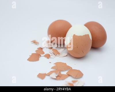 three boiled chicken eggs isolated on white, one of which is peeled Stock Photo