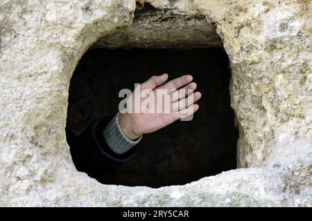 Male hand is visible from the hole in the stone rock. Ancient half-destroyed synagogue. The texture of the old dilapidated masonry. Place for religiou Stock Photo