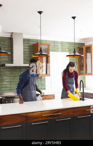 Happy diverse couple cleaning countertop and doing dishes in kitchen at home Stock Photo