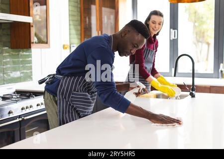 Happy diverse couple cleaning countertop and doing dishes in kitchen at home Stock Photo