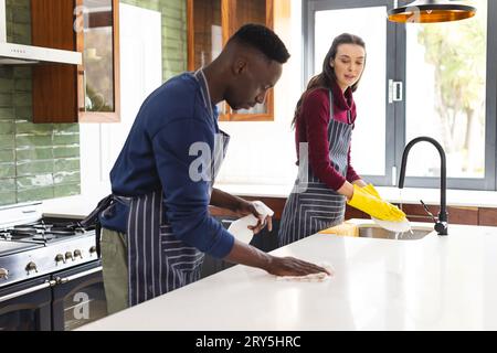 Happy diverse couple cleaning countertop and doing dishes in kitchen at home Stock Photo