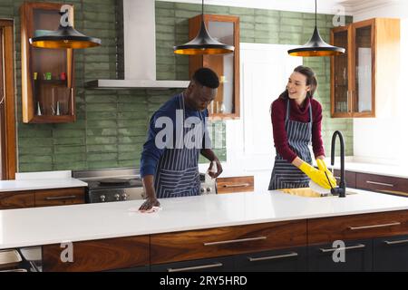 Happy diverse couple cleaning countertop and doing dishes in kitchen at home Stock Photo