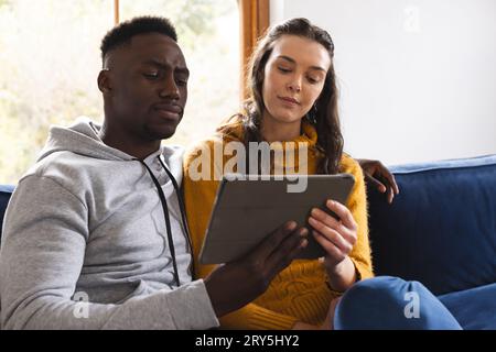 Diverse couple sitting on sofa using tablet at home Stock Photo
