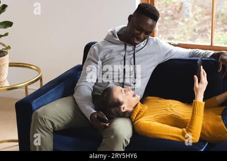Happy diverse couple sitting on sofa using smartphones at home Stock Photo