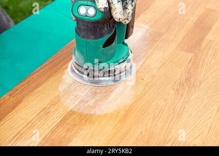 Close up view of person working with sander tool, sanding off stains on old damaged butcher block on oiled wood table. Renovation concept. Stock Photo