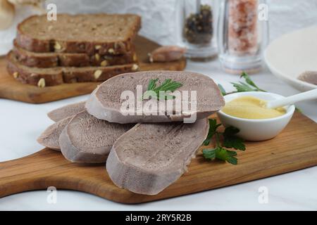 Sliced boiled Beef Tongue Slices on Wooden Board with mustard Stock Photo