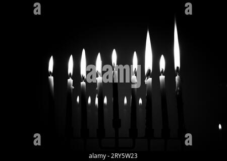 Black and white full menorah on the last night of Hanukkah. All nine candles are lit in a dark room and reflecting in the background. Holiday concept Stock Photo
