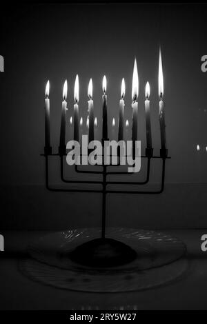 Black and white full menorah on the last night of Hanukkah. All nine candles are lit in a dark room and reflecting in the background. Holiday concept Stock Photo