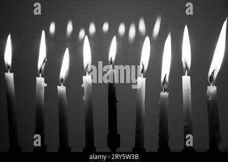 Black and white full menorah on the last night of Hanukkah. All nine candles are lit in a dark room and reflecting in the background. Holiday concept Stock Photo