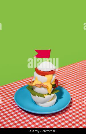 Healthy sandwich. Sliced boiled eggs with bacon, tomato, cheese and lettuce on plate on checkered tablecloth over green background. Breakfast. Pop art Stock Photo